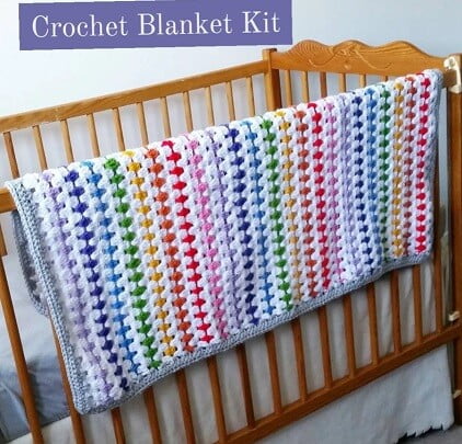 striped blanket in white and rainbow colours is draped over a wooden cot