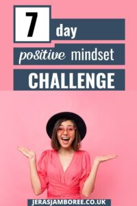 A woman is wearing a hat and dressed in a pink top. Her hands are raised either side of her body and she has a huge smile on her face