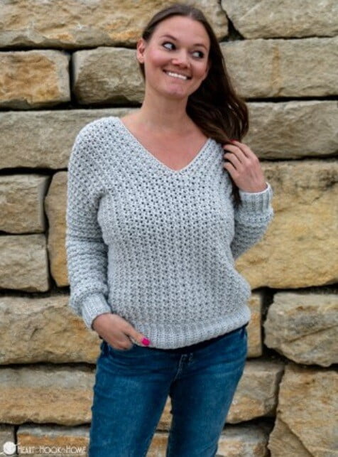 a woman is wearing jeans and a v neck crocheted sweater