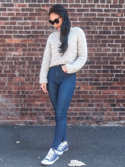 a woman is standing with her hand in a pocket wearing a sweater and denim jeans