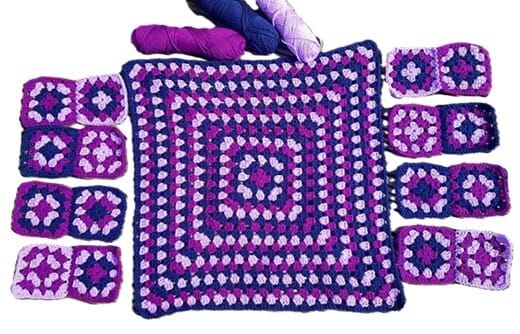 flat lay smaller granny squares on the outside of a larger granny square showing the front (smaller squares) and back (larger square) of a granny square cardigan before assembling