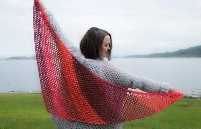 a woman is holding out a Tunisian crochet shawl