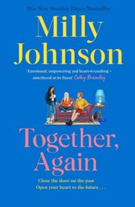 Paperback book cover for Together, Again by Milly Johnson. Two women are sat on a sofa and one is standing. They are drinking a hot drink and chatting. A lamp is lit and there is a rabbit by the side of the sofa