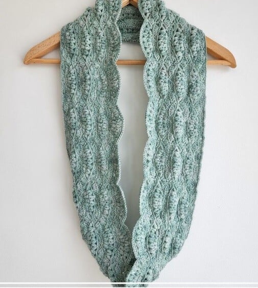 Lightweight and lacy infinity scarf in sage green hung on a clothes hanger