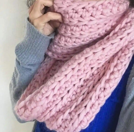 a pink infinity crochet scarf in a chunky yarn wrapped around a woman's neck