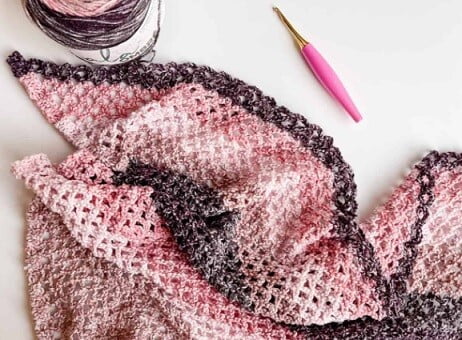 crocheted scarf, hook and yarn cake on a table