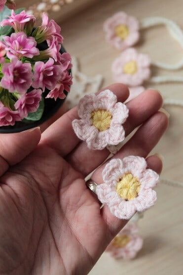 A hand is outstretched with 2 crocheted flowers in the palm