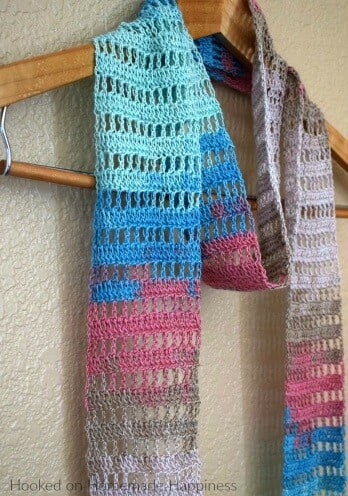 A lacy crochet scarf hanging on a coat hanger in bright colours