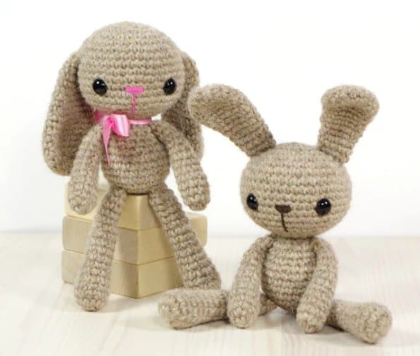 a crocheted bunny with ears down is leaning against a box and another one is sat down with ears straight up