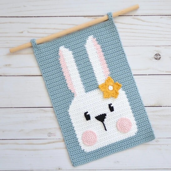 the face of a bunny with a blue background on a crocheted wall hanging