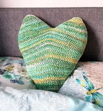 pillow crocheted in the shape of heart in green resting on a bed