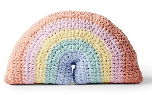 A crochet pillow in the shape of a rainbow in pastel colours