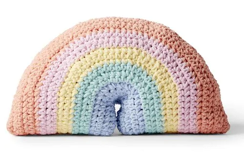 A crochet pillow in the shape of a rainbow in pastel colours