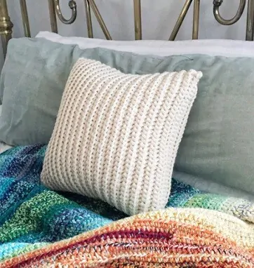 Crocheted pillow in cream is nestled against a headboard and crochet blankets