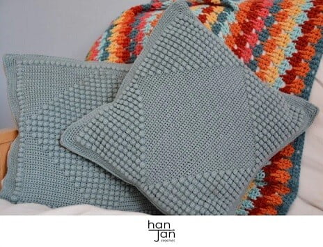 two grey bobble cushions with a crocheted blanket on a sofa