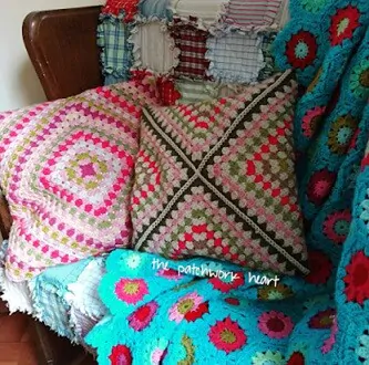 Two bright cushions are on a chair with a granny square blanket