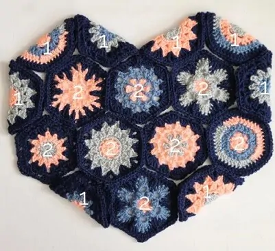 Pillow in blues and pinks crocheted in hexagons into the shape of a heart