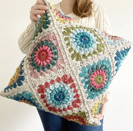 A woman is holding up a pillow made from the sunburst granny square