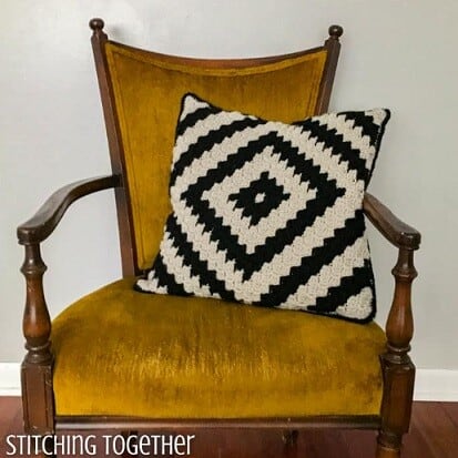 C2C pillow with a geometric design in black and white is nestled on a chair