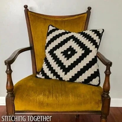C2C pillow with a geometric design in black and white is nestled on a chair