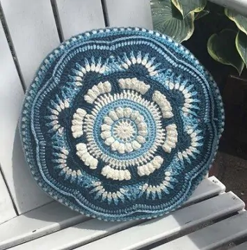round mandala cushion in blues on a white benche