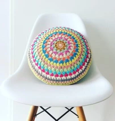 round granny pillow with each round crocheted in different colours on a white chair