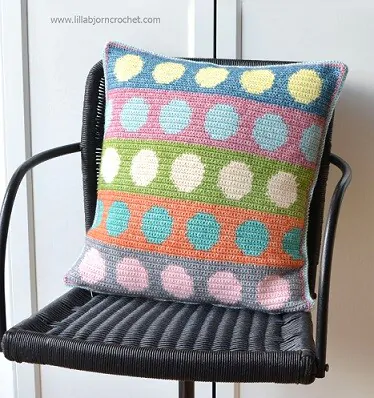Multi coloured pillow with bands of circles nestled on a chair
