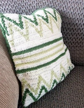 crocheted cushion with a cream background and lighter/darker green chevrons and stripes