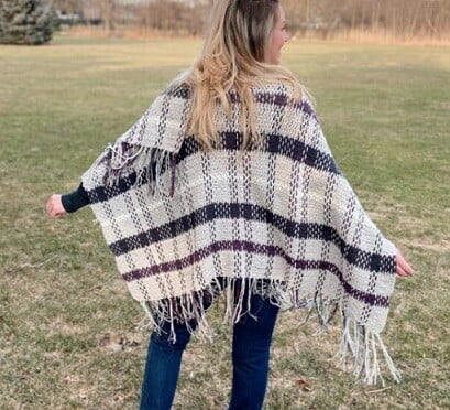 The back view of a women in a field with her arms outstretched wearing a poncho and jeans