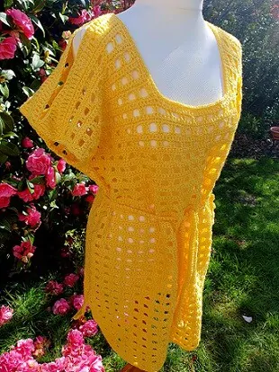 front view of a yellow crocheted beach cover up on a mannequin with pink flowers in the background