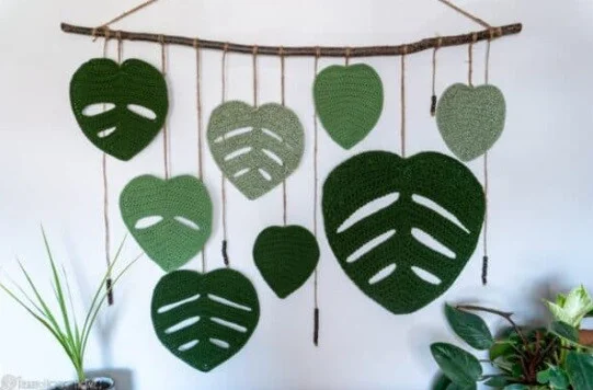different sized leaves in different shades of green are attached to a dowel rod and hanging from a wall
