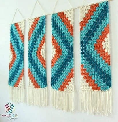 A modified granny square is the pattern in blues and orange for this striking wall hanging