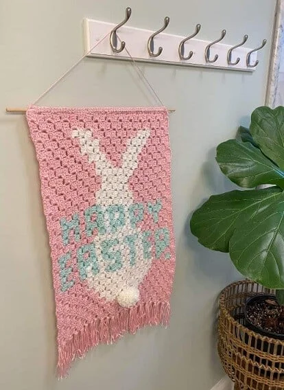 This wall decor is crocheted with the corner-to-corner technique in pink and white and says 'happy Easter'