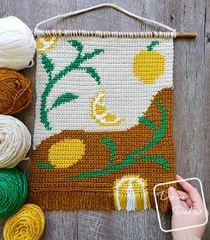 Crochet wall decor of lemons and leaves with white, brown, green and yellow balls of yarn