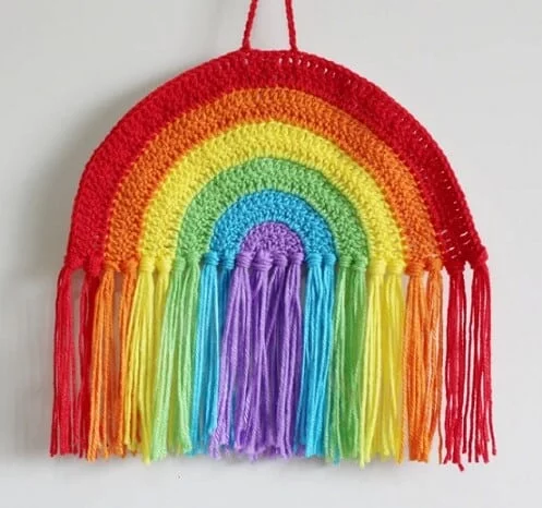 a crochet wall hanging in bright rainbow colours with a rainbow fringe