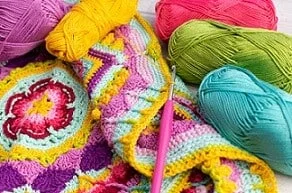 Colorful skeins of yarn arranged next to a crocheted blanket