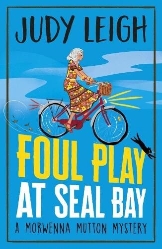 book cover for Foul Play at Seal Bay by Judy Leigh.  A woman is cycling.  The bikes lights are on and a black cat is diving away from the front wheel