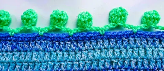 A close up of a pom pom border on a crochet blanket