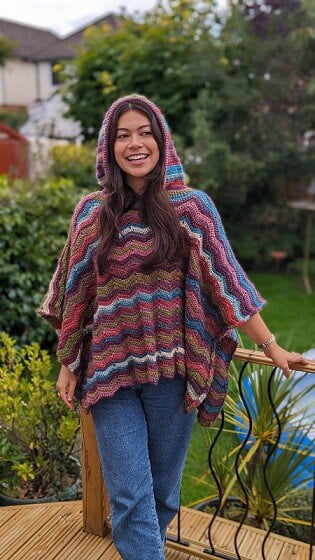 A young woman is smiling wearing a hooded poncho and jeans