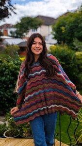 A woman is standing on a decking wearing a crochet poncho