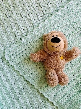 crochet afghan for baby crocheted in a mint colour with a soft toy placed on the flat blanket