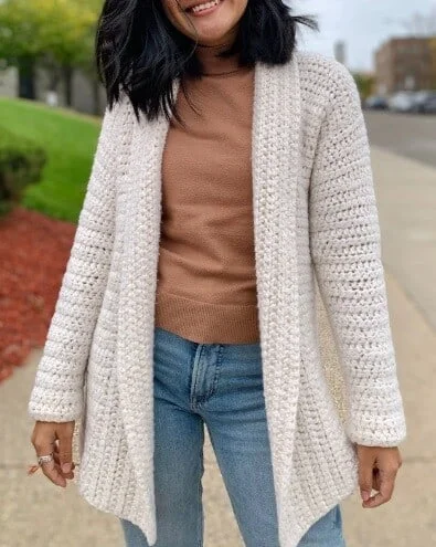 A chunky crochet cardigan is styled on a woman wearing a brown tshirt and jeans