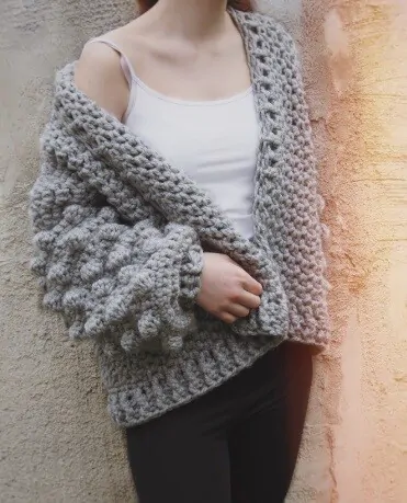 A woman is wearing a white tshirt, jeans and an oversized crochet cardigan