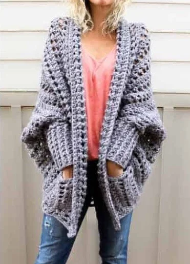 A woman is standing with her hands in pockets on a chunky cocoon cardigan