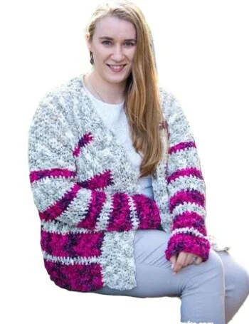A woman is sat down.  She is wearing a striped oversized crochet cardigan