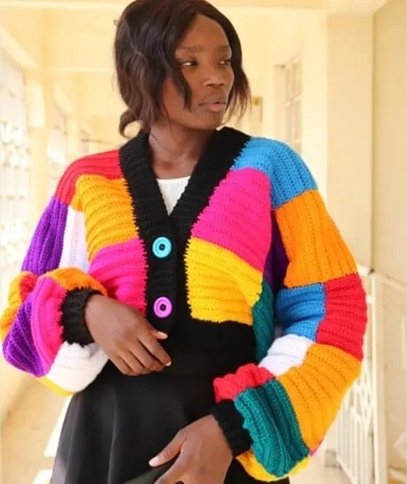 A woman is wearing a bright cardigan crocheted in patchwork