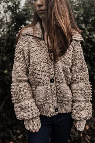 A woman is wearing a chunky cardigan crocheted in the same colour of patches