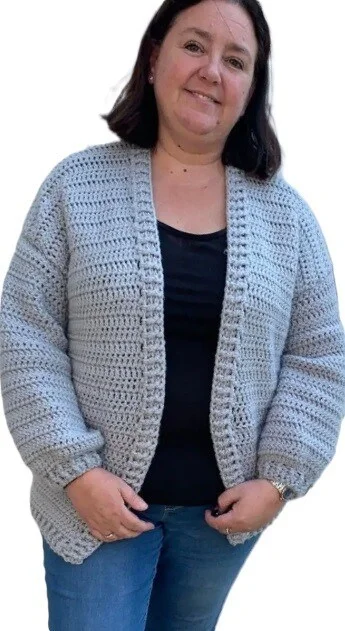 A woman is wearing a black tshirt, jeans and a chunky cardigan