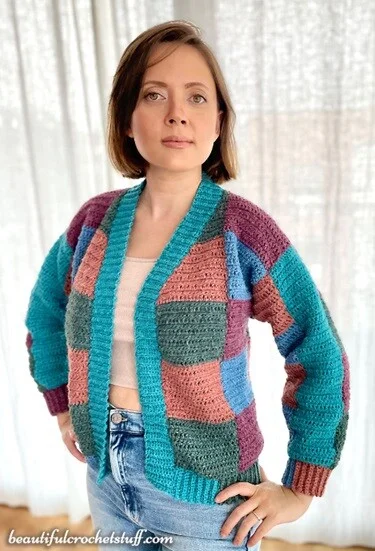 A woman is standing with her hands on her hips wearing jeans and a patchwork cardigan