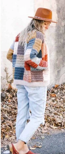 A woman walkimg away is wearing a hat, jeans and a patchwork cardi
